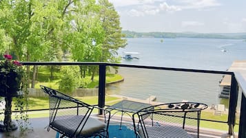 Un balcón con dos sillas de metal y una mesa, con vista a un lago con barcos y vegetación.