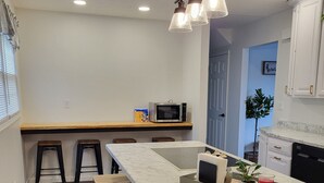 A modern kitchen with a marble countertop, wooden stools, a microwave, and a hanging light fixture.