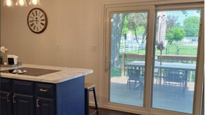 A kitchen with dark blue cabinets, a white countertop, and a large sliding glass door leading to an outdoor patio area with a table and chairs.