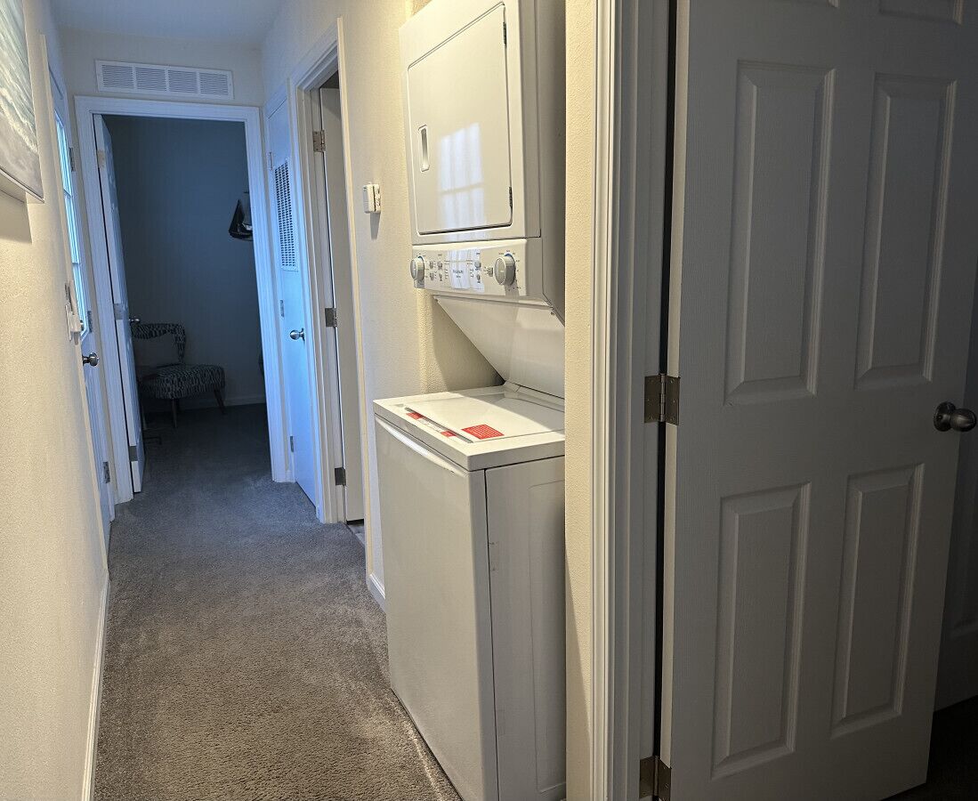 A laundry room with a washer and dryer, a door leading to another room, and a carpeted floor.
