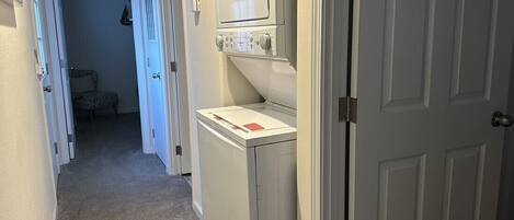 A laundry room with a washer and dryer, a door leading to another room, and a carpeted floor.