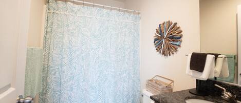 A bathroom with a leaf-patterned shower curtain, a decorative wall piece, a toilet, a sink with a marble countertop, and a towel rack.