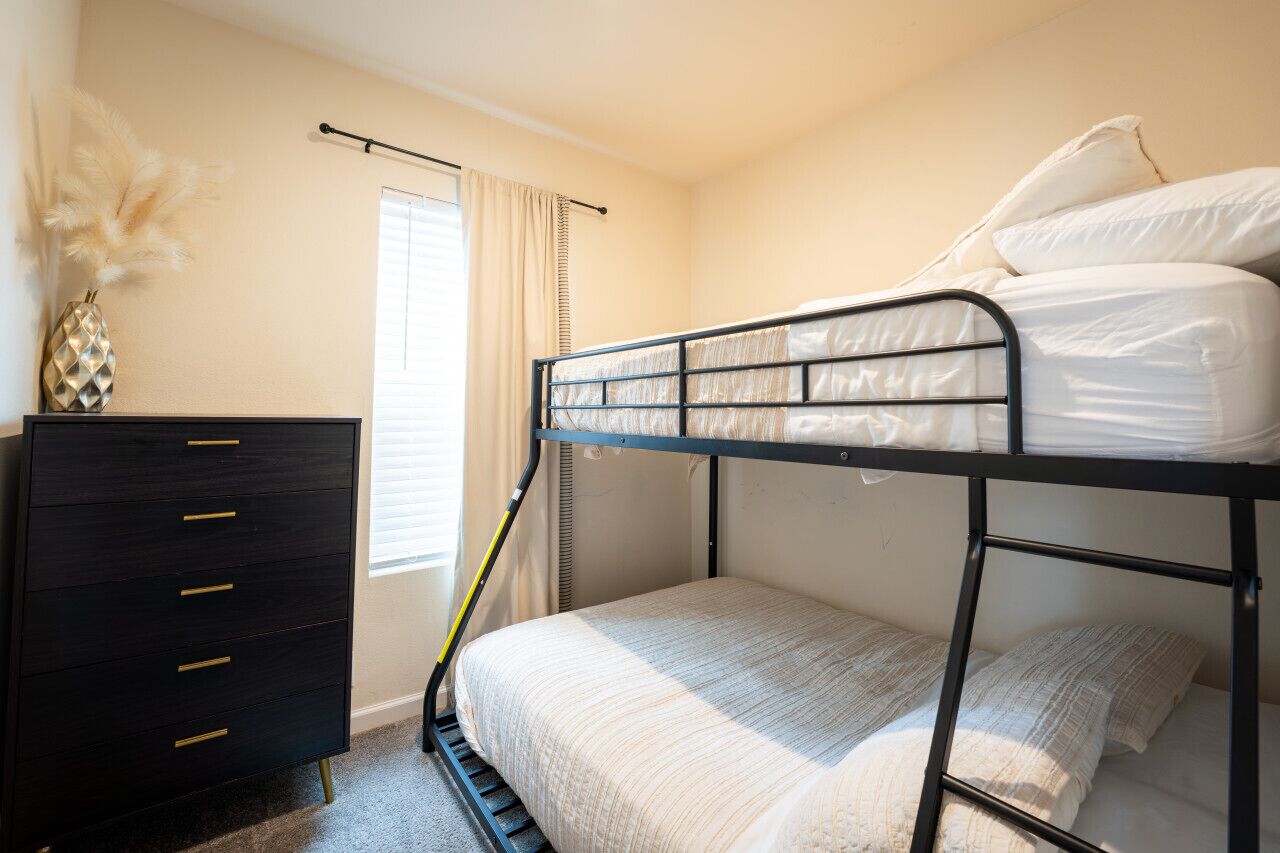 Een slaapkamer met een stapelbed, een zwarte dressoir en een raam met gordijnen.