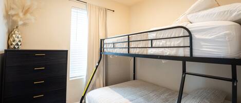 Een slaapkamer met een stapelbed, een zwarte dressoir en een raam met gordijnen.