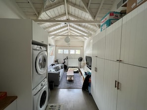 A laundry room with stacked washers and dryers, a sofa, a fan, and a television.