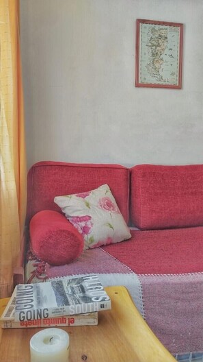 Un sofá rojo con un cojín floral, un mapa enmarcado en la pared y un libro titulado 'Going South' sobre una mesa de madera.