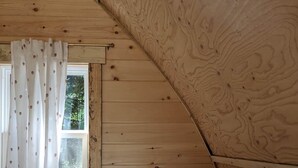 Ein Schlafzimmer mit schrägverdeckter Decke, einem Fenster mit Vorhang und einer gesteppten Bettdecke.