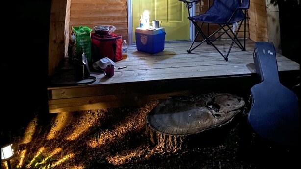Ein gemütliches Holzhaus mit Veranda, einem blauen Klappstuhl und einem kleinen Tisch mit Gegenständen darauf.