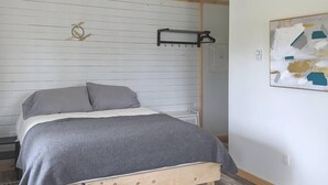 A bedroom with a bed, a wall-mounted coat rack, and a painting. - Aurora Cottage At The Spruces (Ingonish)