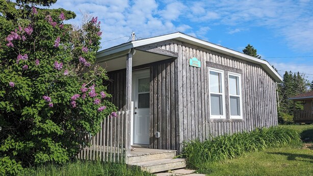 A small wooden cabin with a porch, a door, and a sign indicating it is a guest house. - Aurora Cottage At The Spruces (Ingonish)