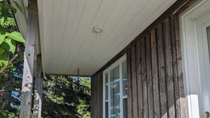A covered porch with a table and chairs, a barbecue grill, and a door. - Aurora Cottage At The Spruces (Ingonish)