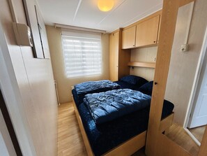 A compact bedroom with a bed, a window with blinds, and wooden furniture.