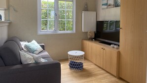 Un soggiorno moderno con un divano grigio, una televisione su un mobile in legno, un termosifone e una finestra con vista sul verde.