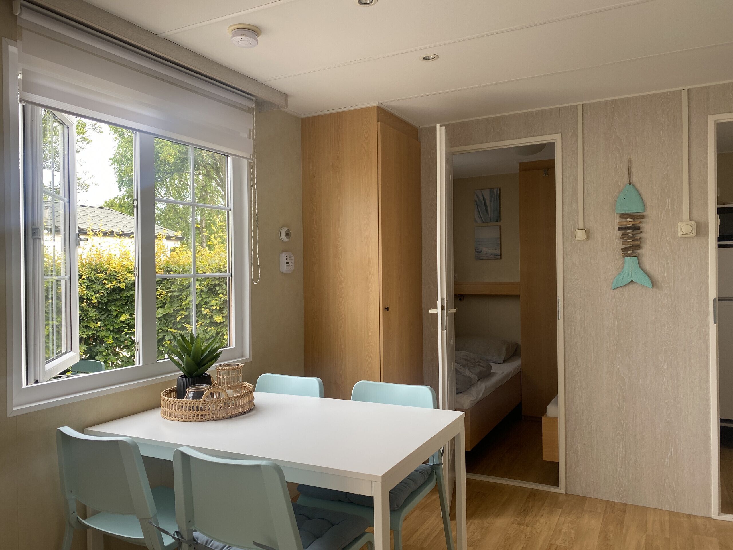 A room with a dining table, chairs, a potted plant, a bed, and a wall-mounted fish decoration.