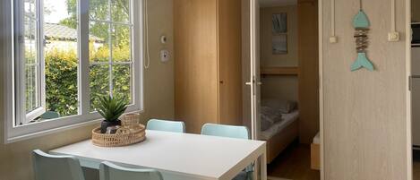A room with a dining table, chairs, a potted plant, a bed, and a wall-mounted fish decoration.