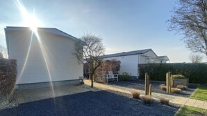 Un immobile residenziale con garage, patio attrezzato con panchina e giardino con siepi e recinzione in legno.