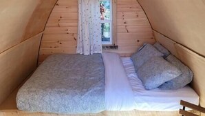Une petite chambre mansardée, chaleureuse et accueillante, avec un plafond en pente, un lit simple avec des oreillers et une fenêtre agrémentée de rideaux.