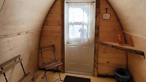 Une petite pièce mansardée, chaleureuse, avec un plafond en pente, un banc en bois, une petite chaise pliante, une porte avec un rideau et une étagère sur laquelle est posée une lanterne.