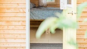 Una habitación pequeña de madera con una cama, una ventana con cortinas y una puerta.