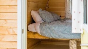 Una cabaña de madera pequeña y acogedora, con una cama individual, un cartel que dice “JACK ROOM” y una ventana con cortinas.