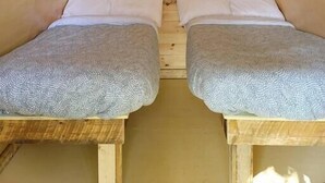Pequeño dormitorio en ático, con forma triangular, con dos camas, paredes de madera y una ventana con cortina.
