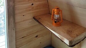 Una pequeña habitación de madera con techo inclinado, un estante de madera y un farol.