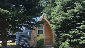 Eine kleine, eingeschossige Holzhütte mit geneigtem Dach, umgeben von dichtem Wald.