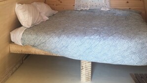 Ein kleiner, gemütlicher Raum mit schrägen Wänden, einem Einzelbett mit gemustertem Bettbezug, einem Kopfkissen und einem Vorhang mit Punkten.