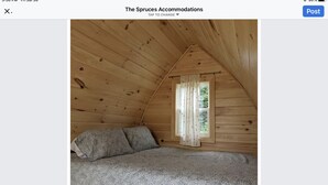 Una habitación acogedora con techo de madera, ventana con cortinas y cama con ropa de cama estampada.