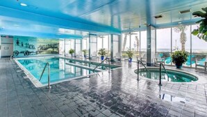 Ein Innenpool mit klaren Glaswänden, einem gefliesten Boden und Blick auf Palmen im Freien.
