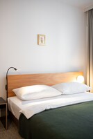 Cama bem arrumada com roupa de cama branca e manta verde, luminária de cabeceira e quadro na parede.
