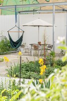 An outdoor patio with a table and chairs, a hanging hammock, and a potted plant.