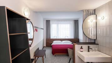 Hotelkamer met een bed, bureau, kledingkast, badkamer met wastafel en spiegel, en een raam met gordijnen.