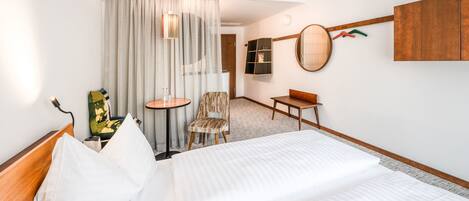 Habitación de hotel con una cama grande, una silla, una mesita y un televisor montado en la pared, además de una cortina.