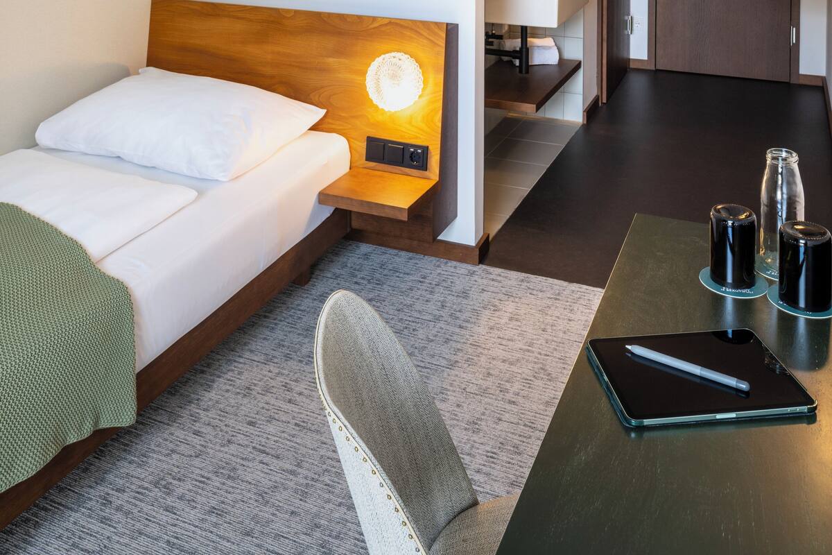 A hotel room with a bed, a desk, a chair, a bathroom, and a kitchenette.