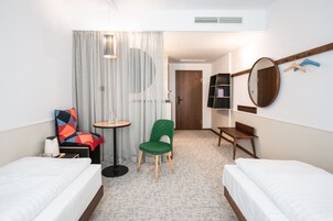 Una camera d'albergo con due letti, un piccolo tavolo rotondo, una sedia verde, uno specchio e una libreria.