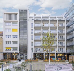 A modern multi-story building with balconies, a small tree in the foreground, and a sign advertising a buffet.