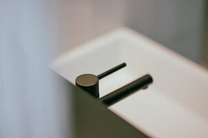 Uma casa de banho moderna e minimalista, com uma torneira preta elegante e um dispensador de sabonete cilíndrico.