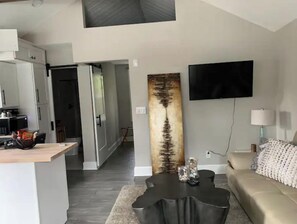 A modern living room with a sofa, a coffee table, a flat-screen TV, and a large abstract painting. - Adorable Cottage in Downtown Aiken (Aiken)