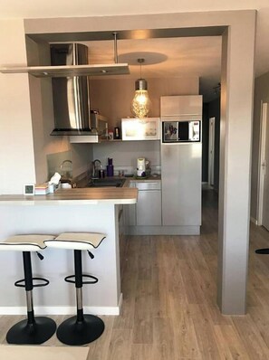 Cozinha moderna com eletrodomésticos de aço inoxidável, bancada de madeira e dois banquetas pretas.