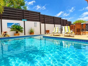 A clear blue pool with lounge chairs and a wooden fence.