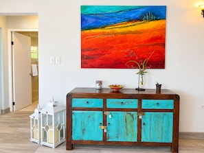 A room with a teal-colored cabinet, a colorful abstract painting, and a vase with flowers on the wall.