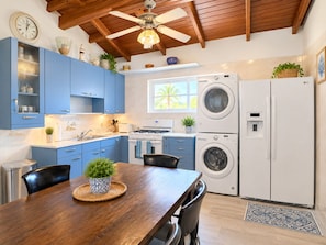 A modern kitchen with blue cabinets, a wooden dining table, and a ceiling fan.