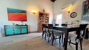 Een eethoek met een houten tafel en stoelen, een kast met glazen deuren, en een schilderij aan de muur.
