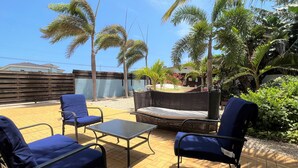 Een terras met blauwe stoelen en een tafel, omgeven door palmbomen en groen.