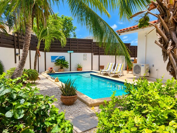 A swimming pool with lounge chairs, surrounded by tropical plants and palm trees.