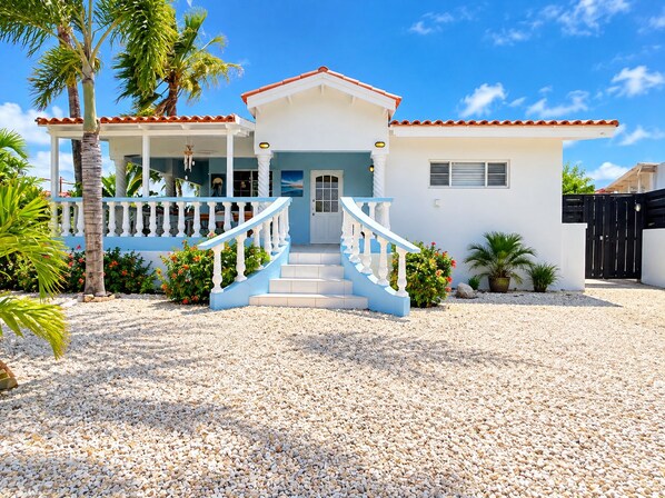 A two-story house with a white exterior, a red-tiled roof, and a blue staircase leading to the front door.