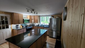 Une cuisine moderne avec des meubles en bois, un grand îlot central, des appareils électroménagers en acier inoxydable et une vue sur l’extérieur.