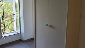 A room with a large wardrobe, a window with a view of greenery, and a door with a handle. - Le Clos de L'arc (Vallon Pont d'Arc)