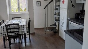A compact kitchen with a dining area, a spiral staircase, and a window with curtains. - Le Clos de L'arc (Vallon Pont d'Arc)
